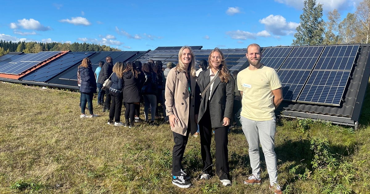Three students smiling at the camera with solar panels in the background.
